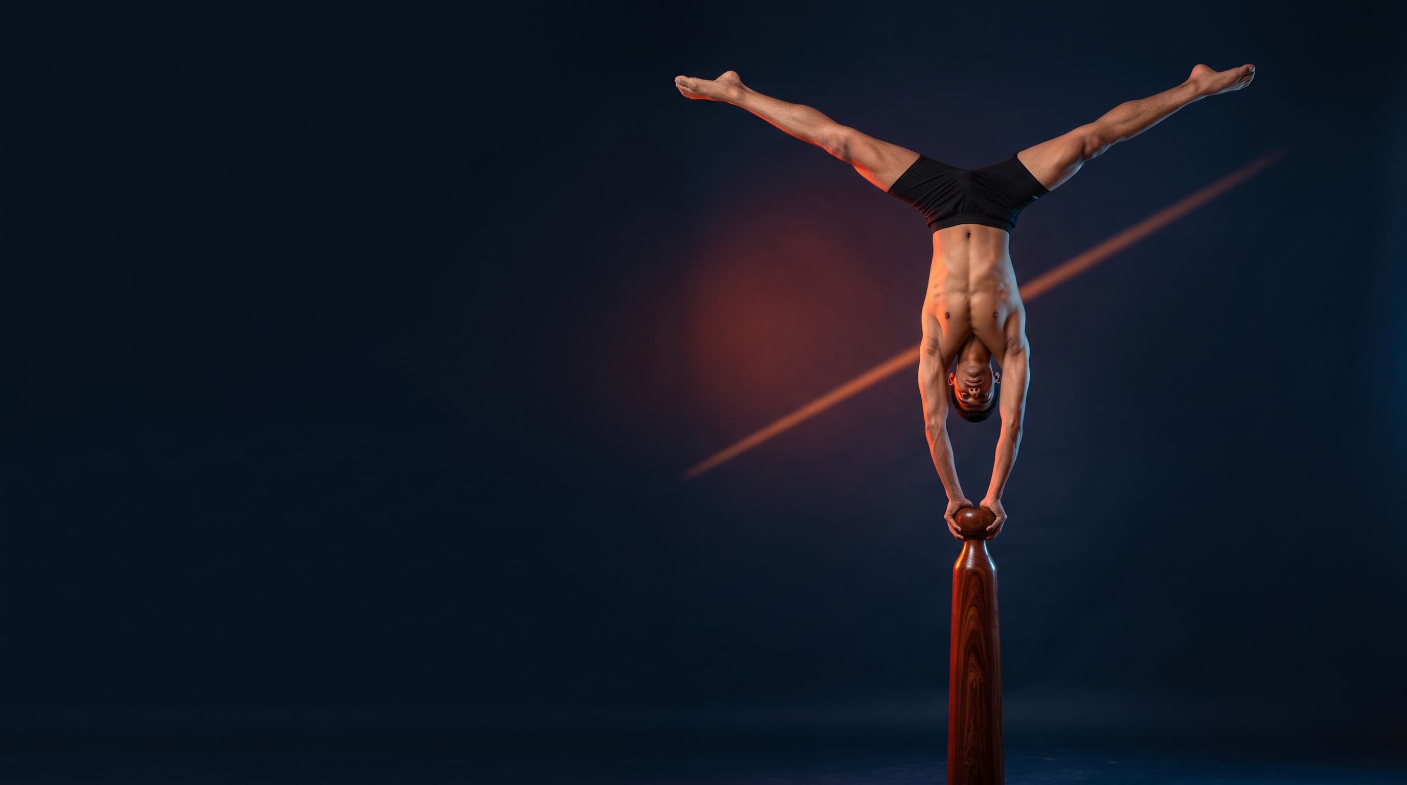 Mallakhamb athlete upside down in a split handstand on top of a wooden pole, lit by a warm streak of light